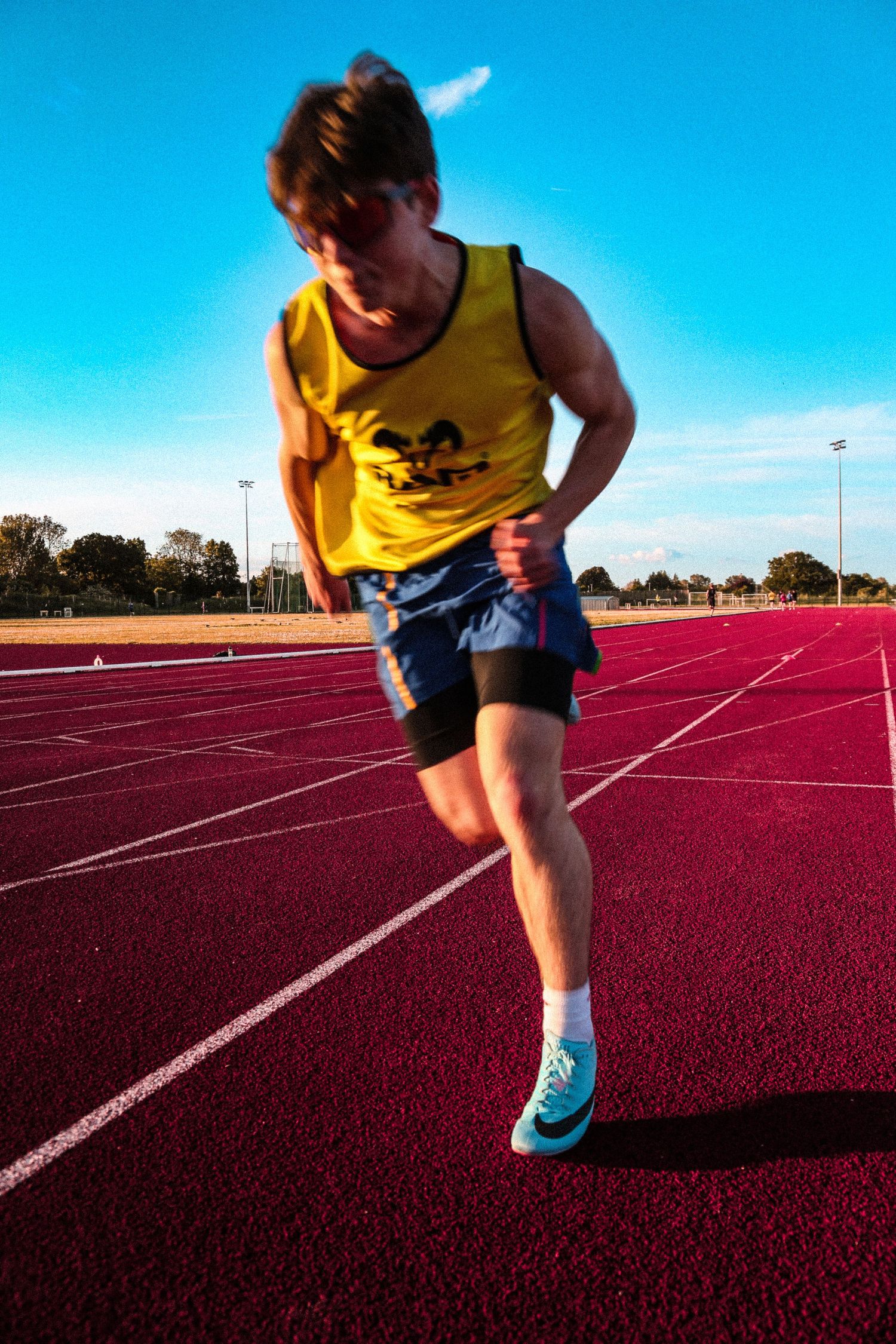 Runner in yellow tank top training on red athletic track.