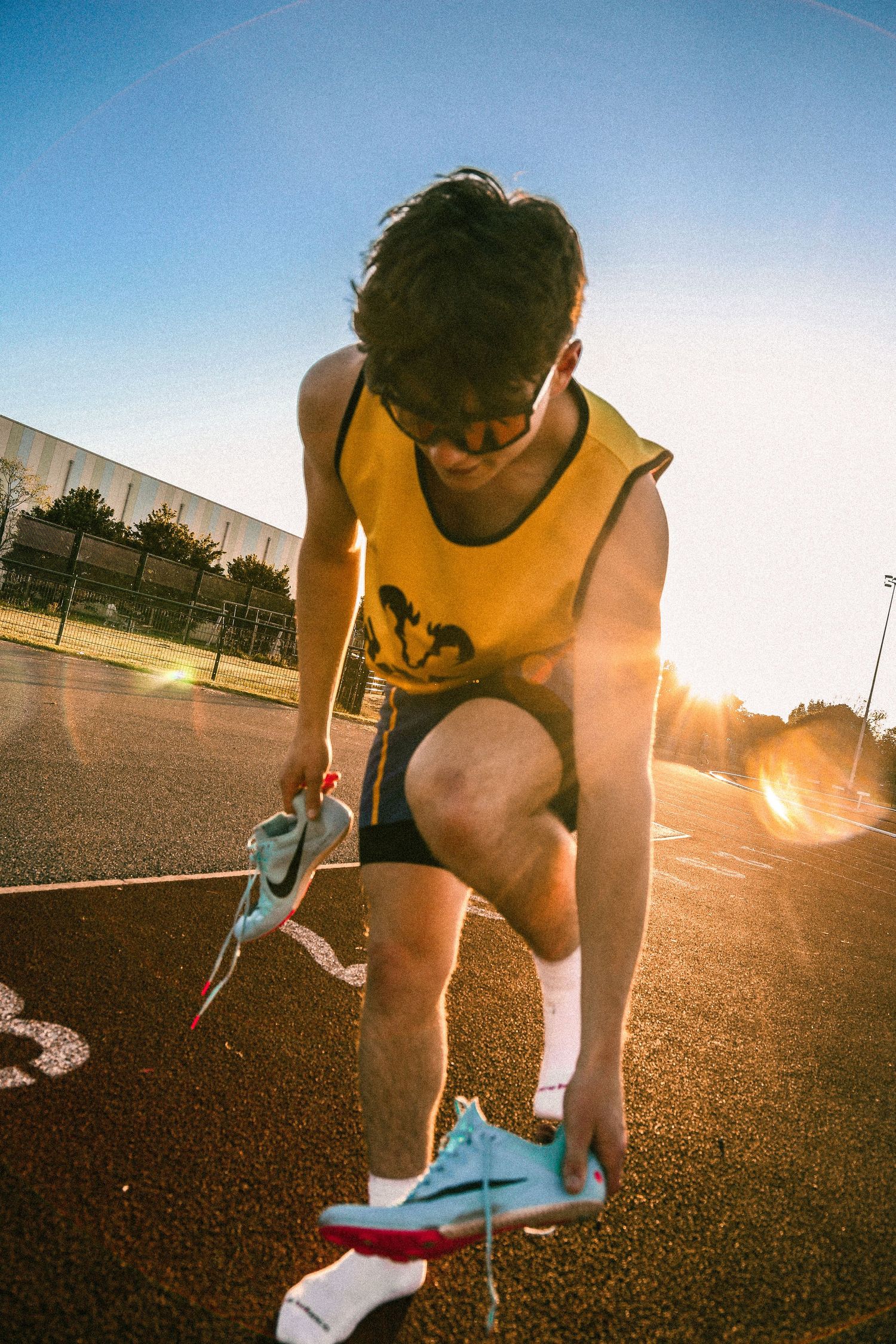 Athlete in yellow tank top tying shoelaces on running track at sunset.