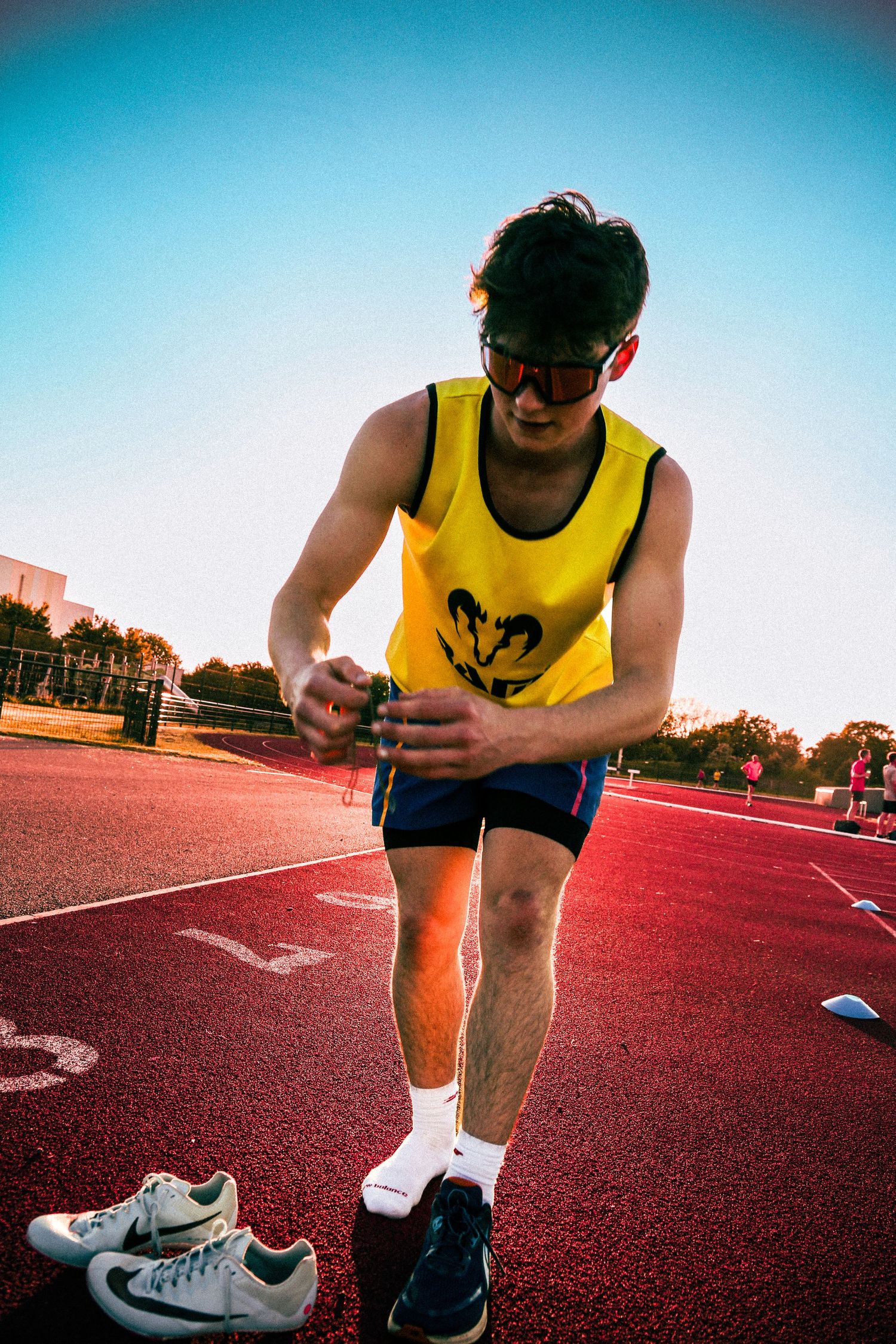 Runner in yellow tank top stretching on red track during training session.
