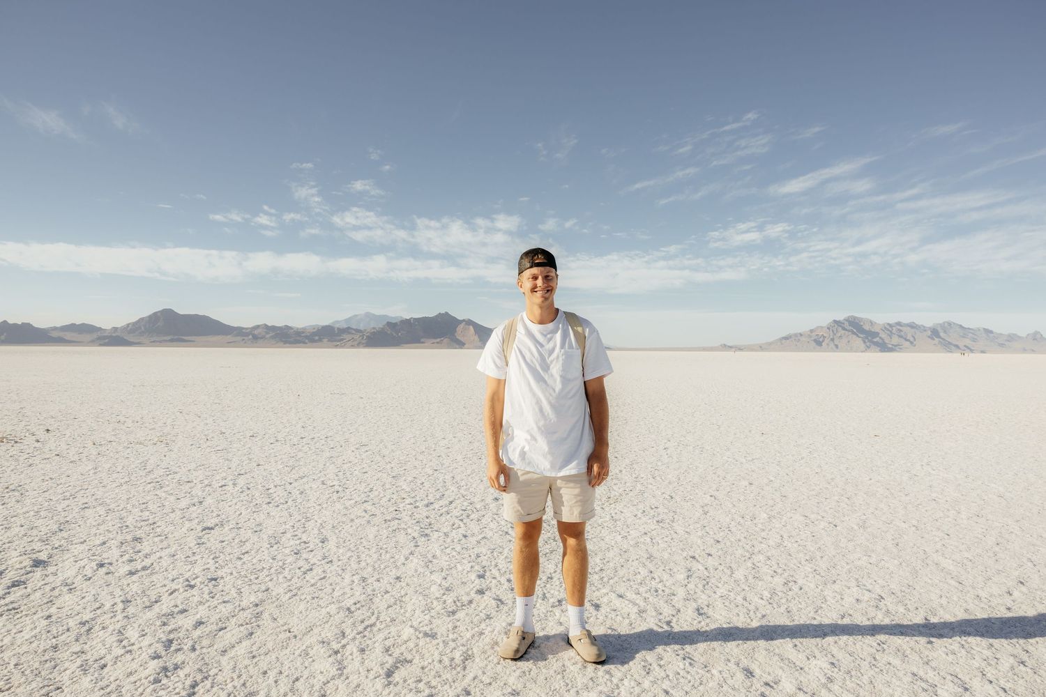 Man in white outfit standing on Bonneville Salt Flats with mountains in background.