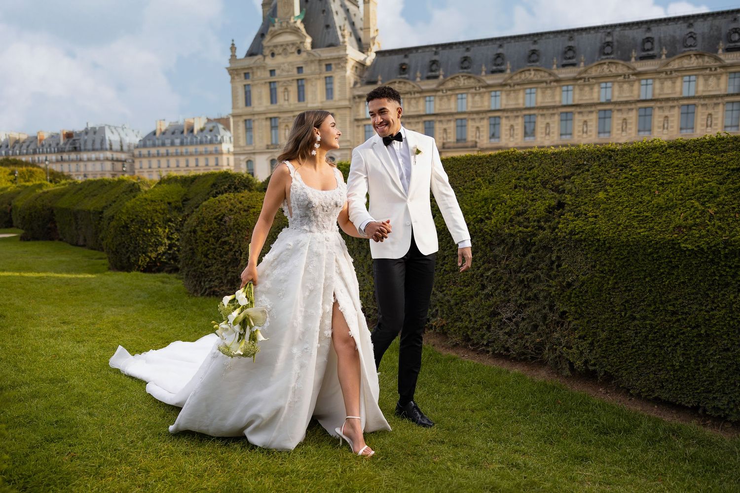 Wedding couple posing in formal attire on manicured garden grounds of elegant estate.