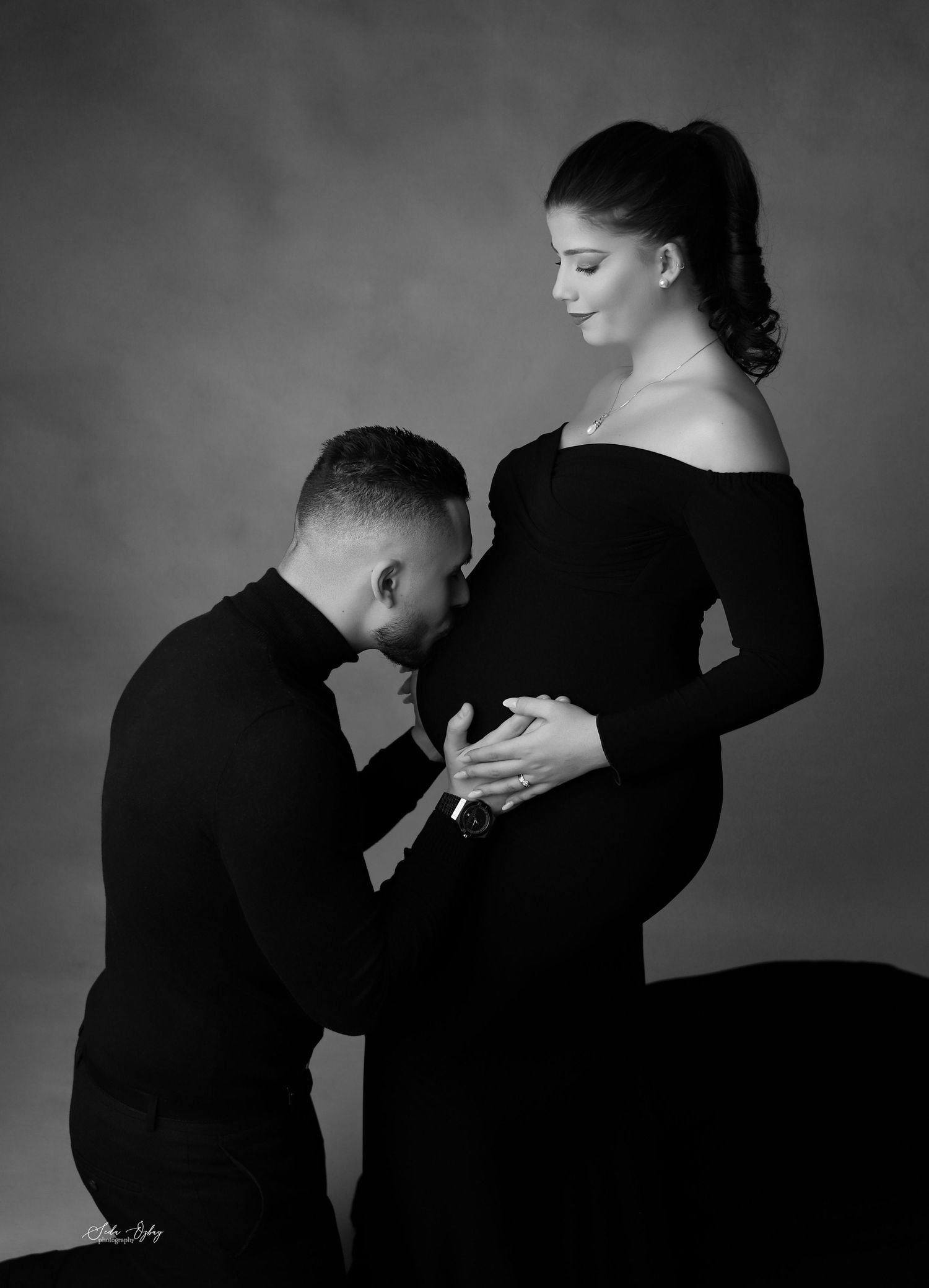 An artistic black and white maternity portrait with an off-shoulder gown.