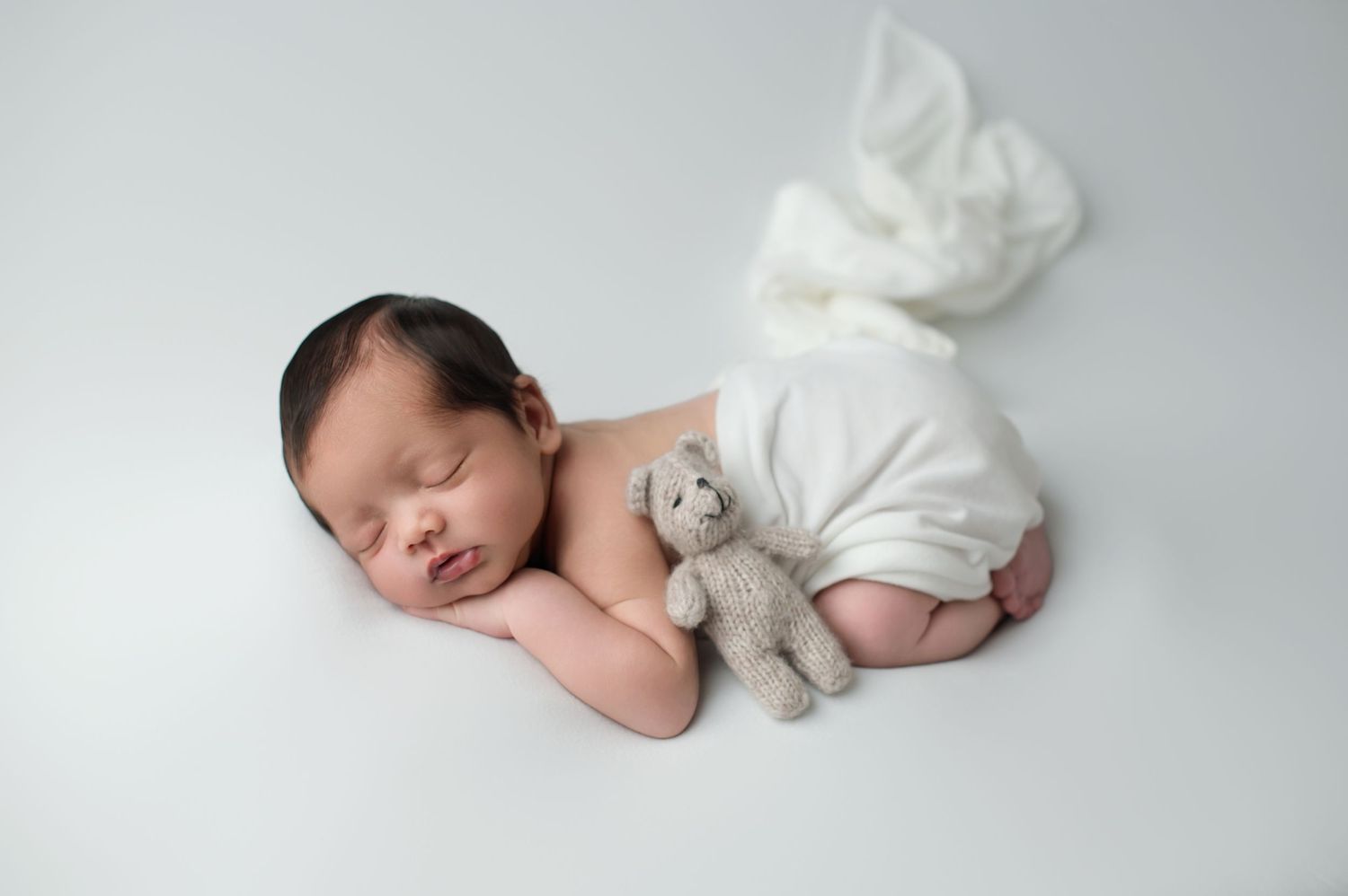 Sleeping newborn baby wrapped in soft brown fabric lies peacefully curled up during professional photo session.
