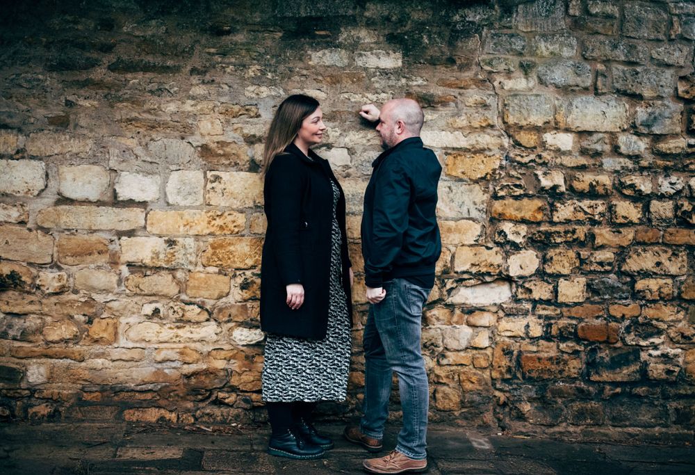A couple gazes at each other while standing in front of an old stone wall.