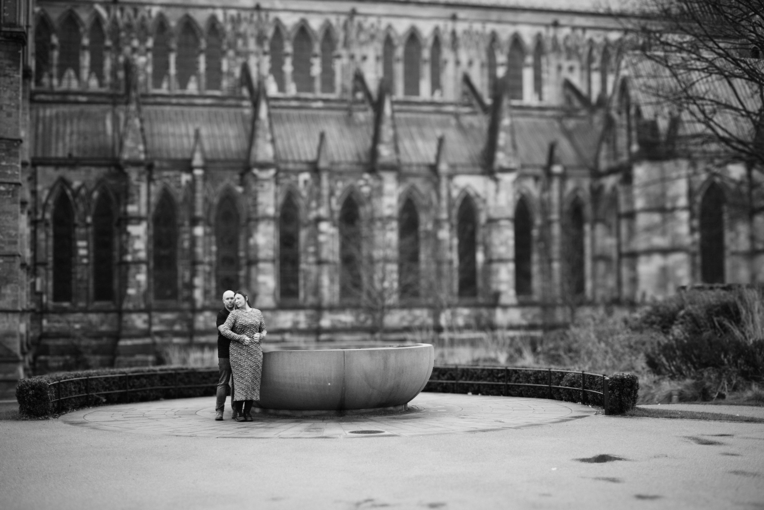 A lone figure stands near a fountain with gothic cathedral architecture in the background.