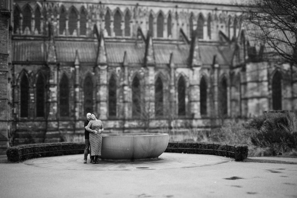 A lone figure stands near a fountain with gothic cathedral architecture in the background.