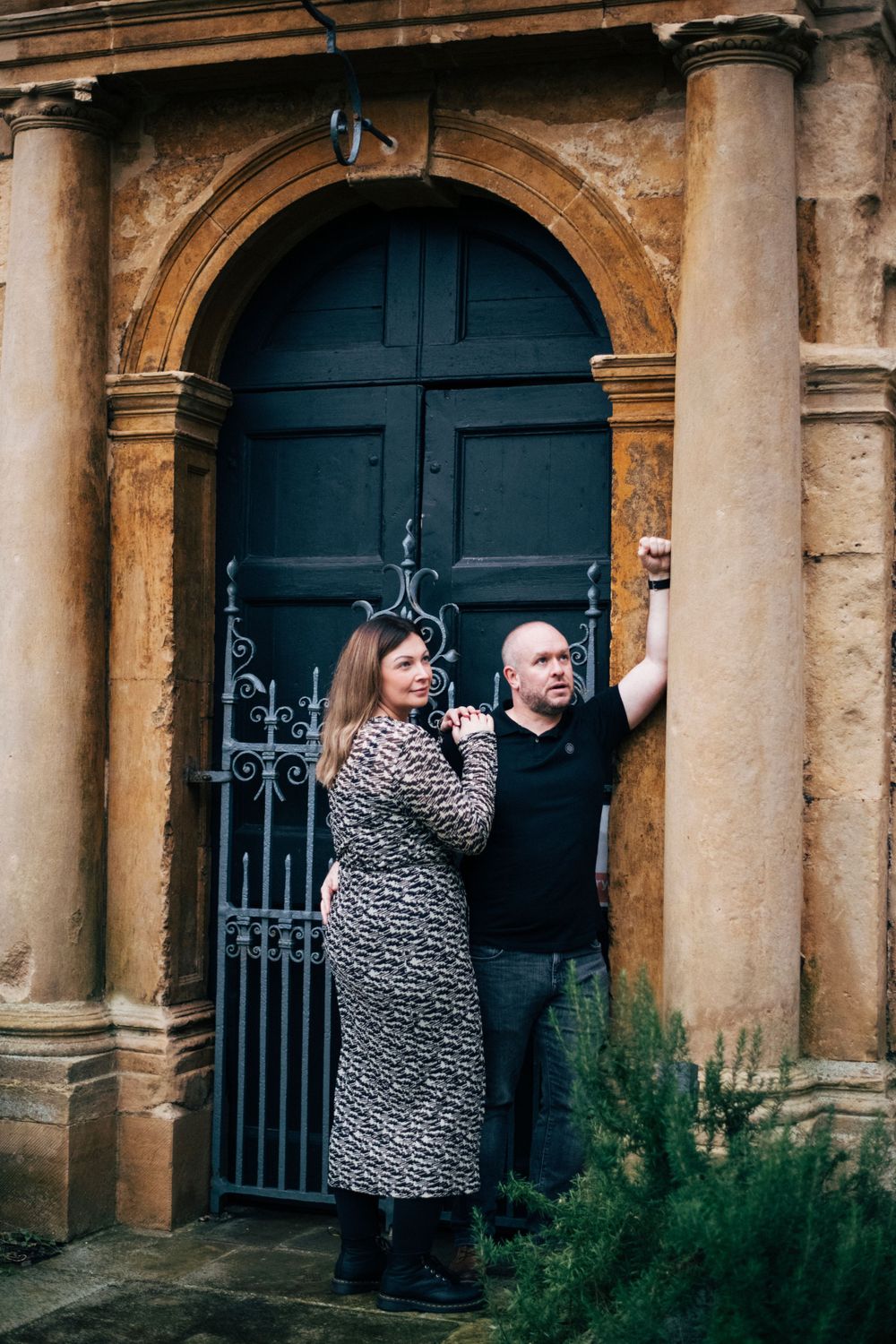 A couple poses in front of an ornate blue door with classic stone columns.