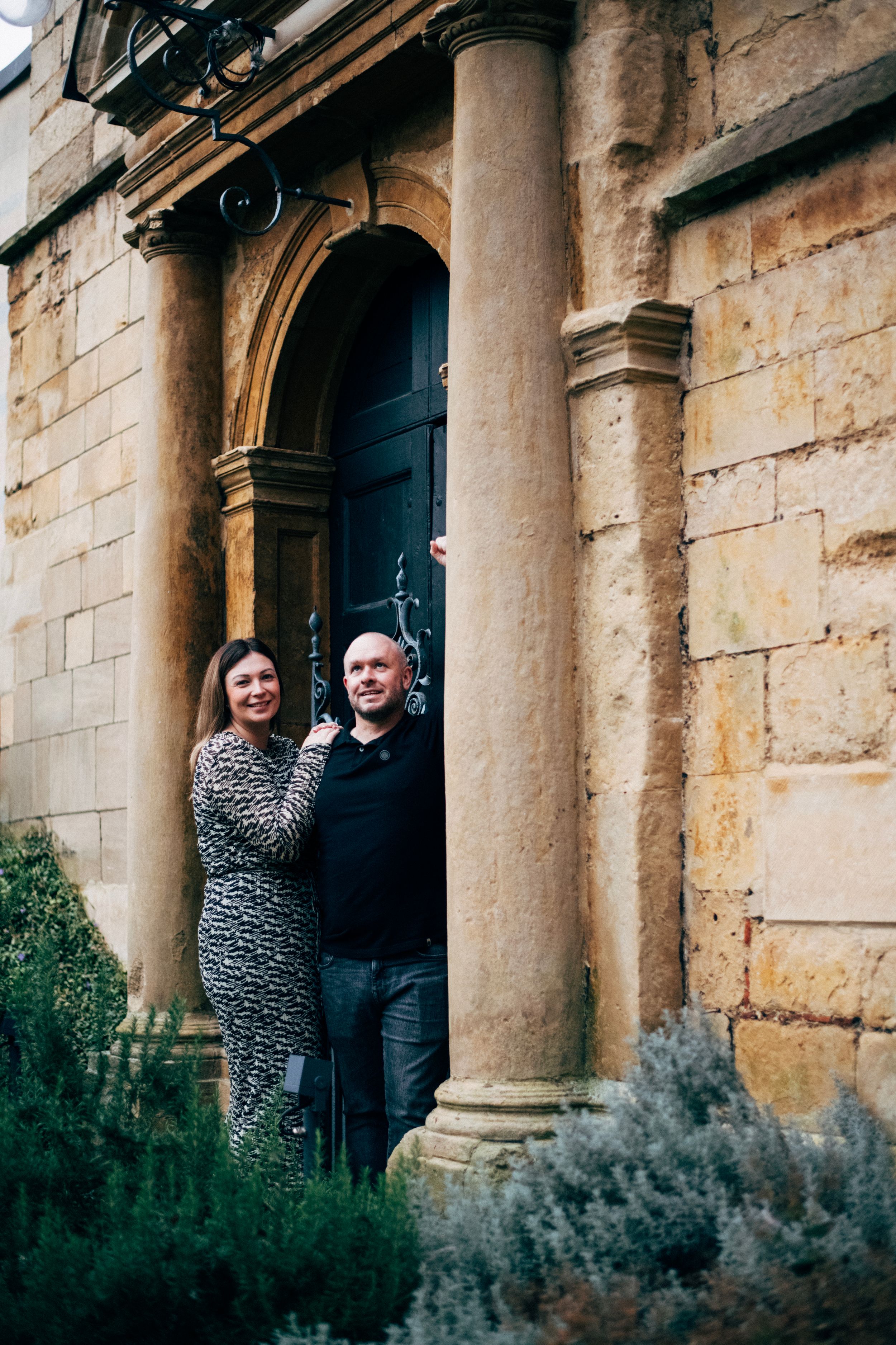 A couple shares a laugh while standing in a historic stone archway entrance.