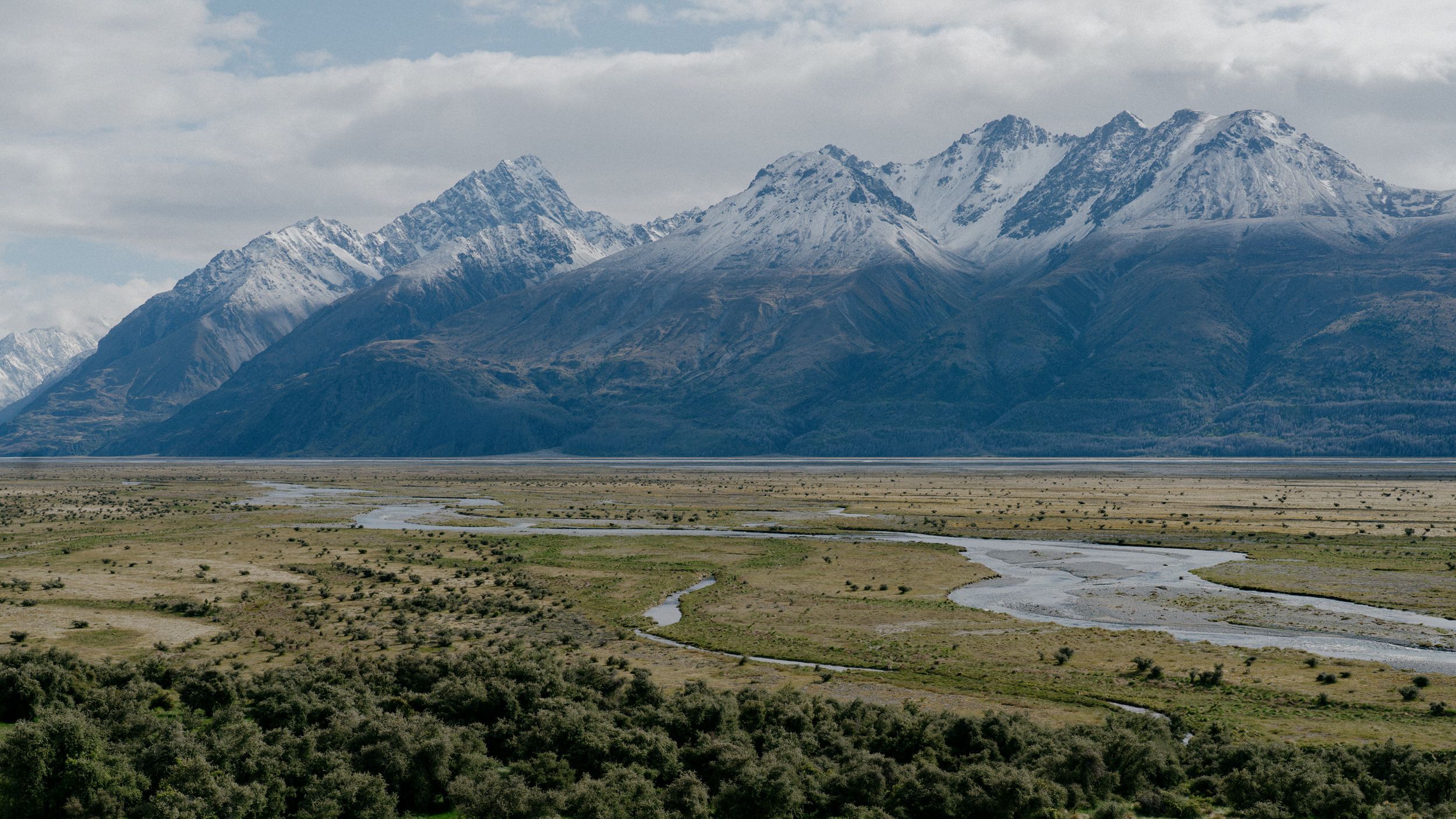 Snow-capped mountain range overlooking a vast plain with meandering river systems.