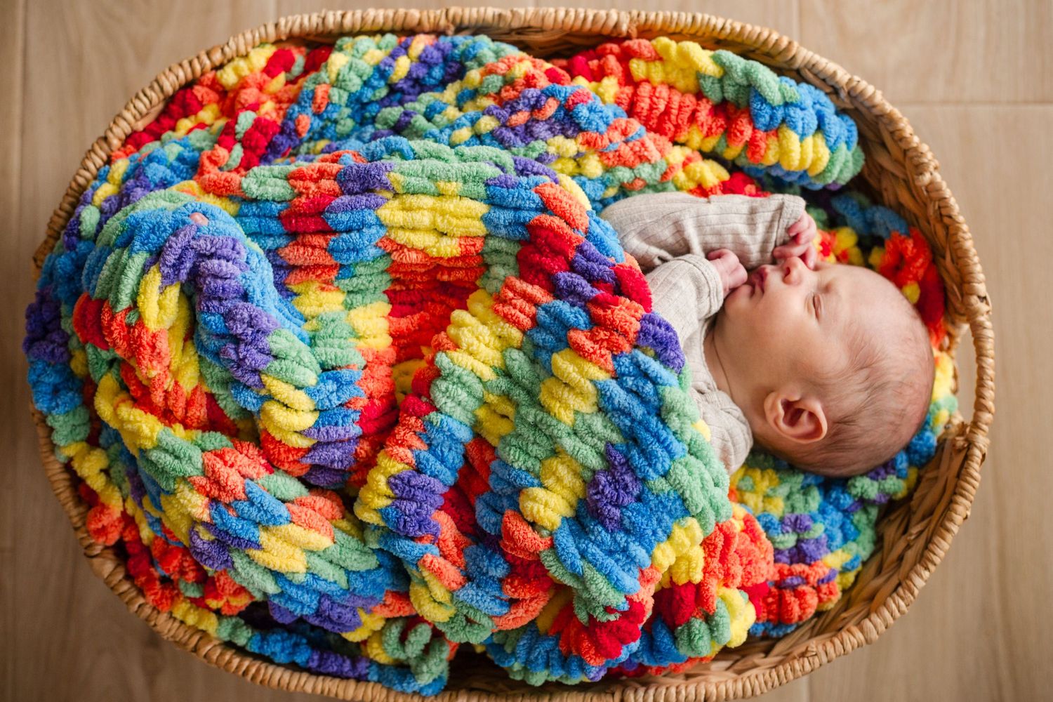 Baby sleeping in colorful knit blanket inside woven basket.
