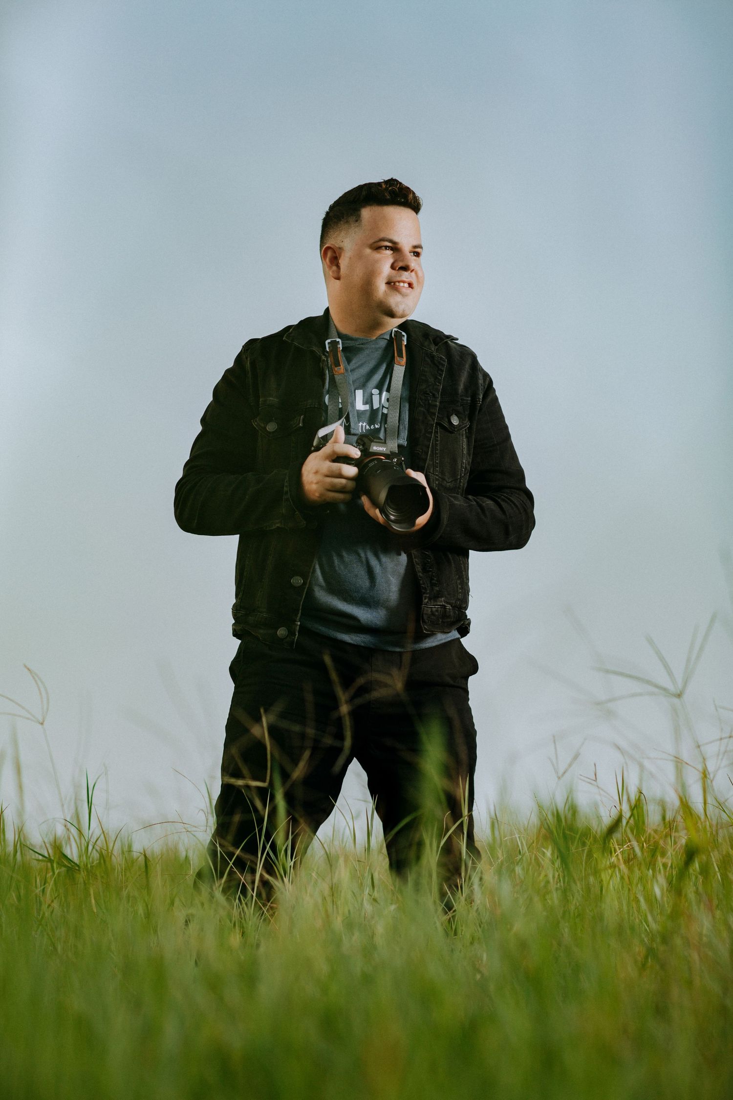 Photographer in black jacket takes photos while kneeling in a grassy field.