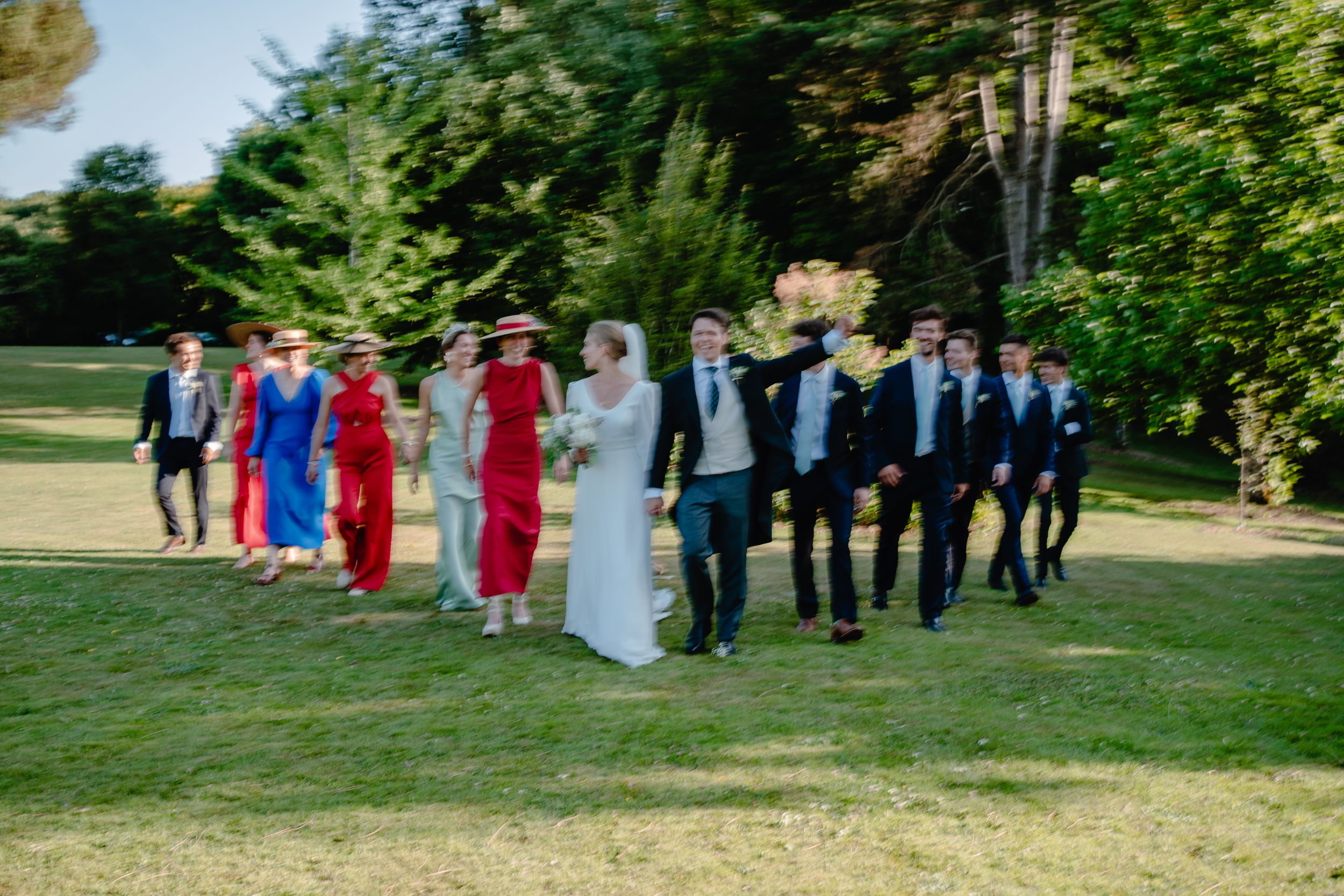 Wedding party walks together across green lawn during outdoor celebration.