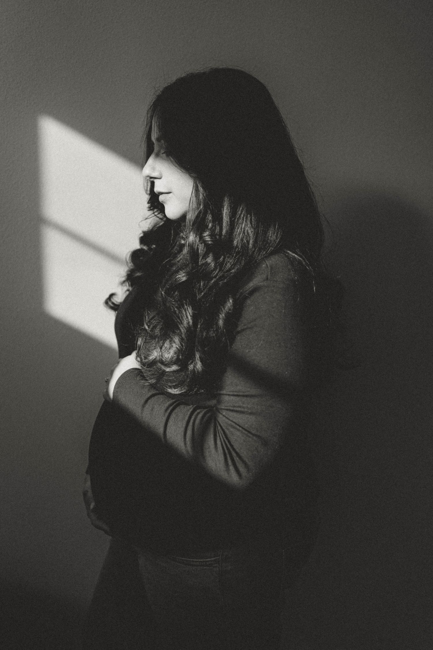 Silhouette of a person in black standing by window in dramatic lighting.