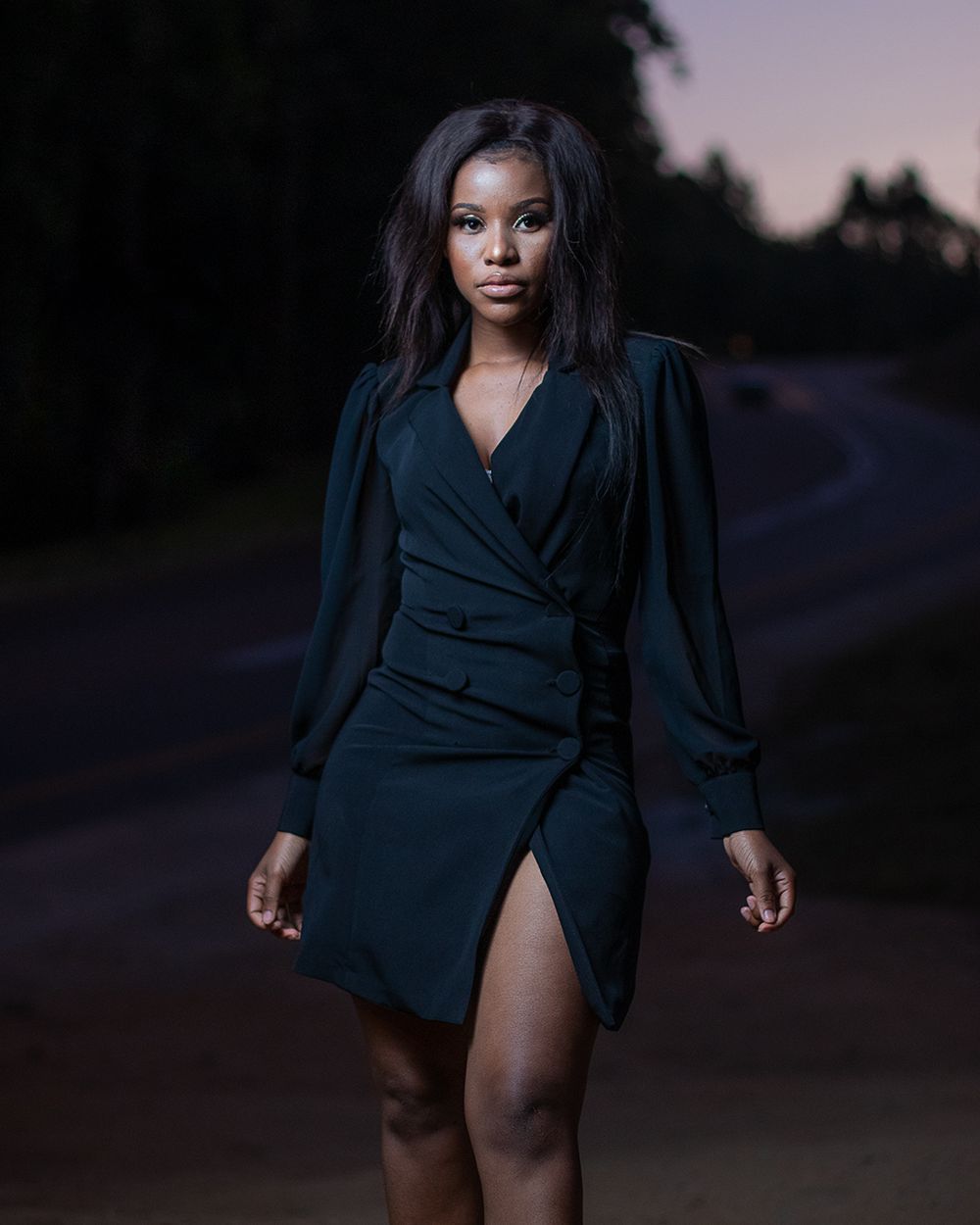 Evening fashion portrait in fitted navy dress on dark rural road.