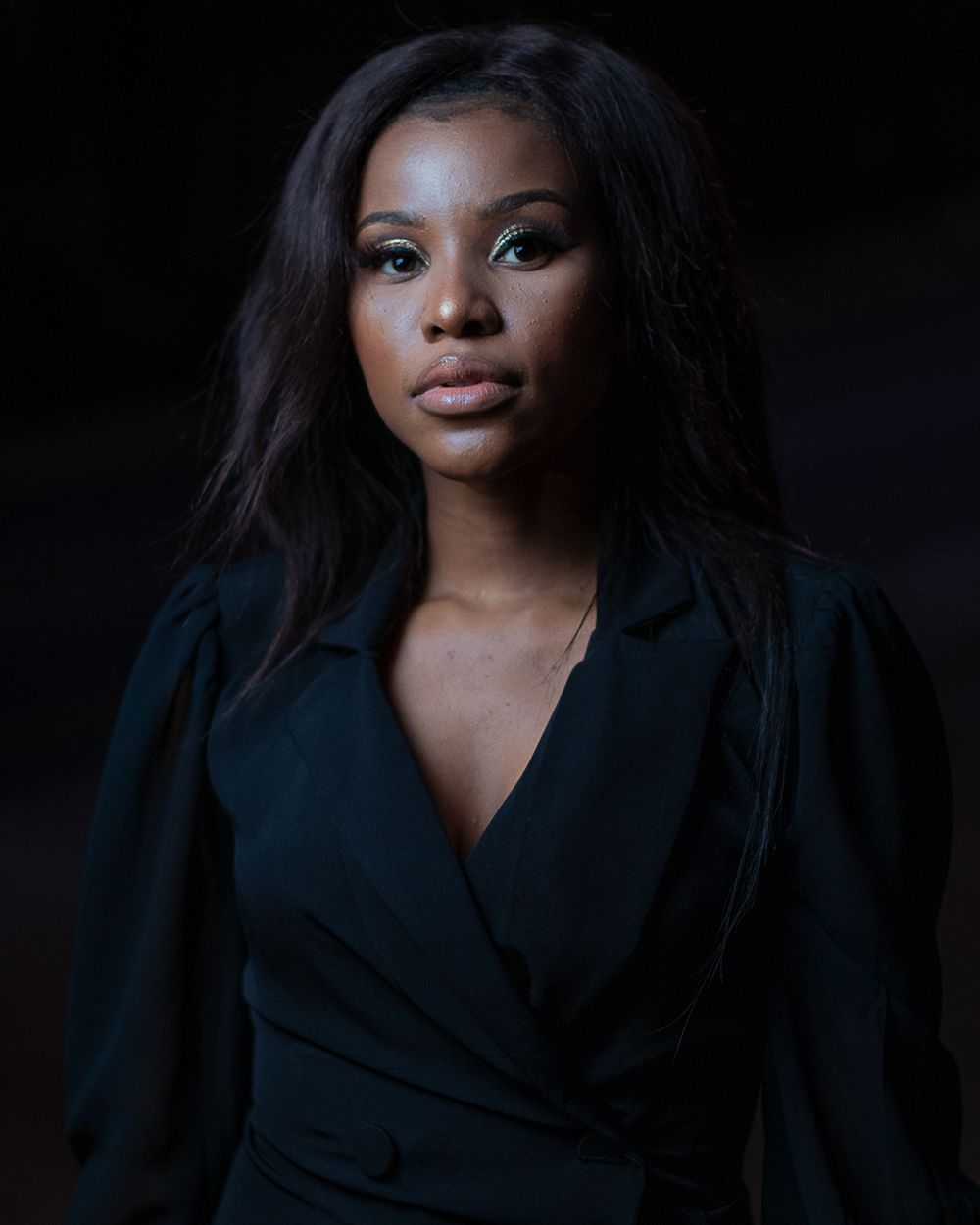 Dramatic portrait in dark lighting featuring elegant black wrap dress.