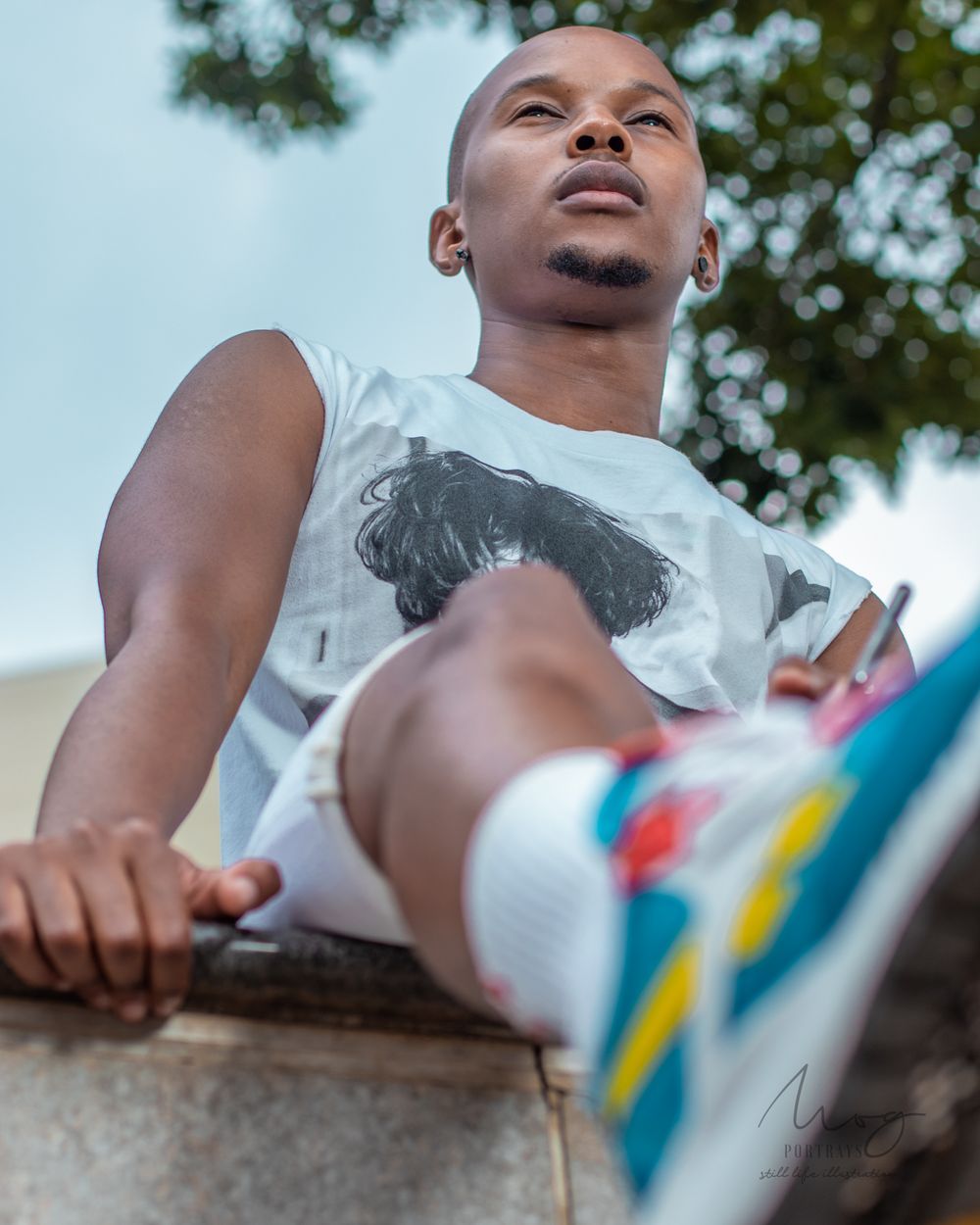 Low angle shot of person in white t-shirt and colorful sneakers sitting on ledge.