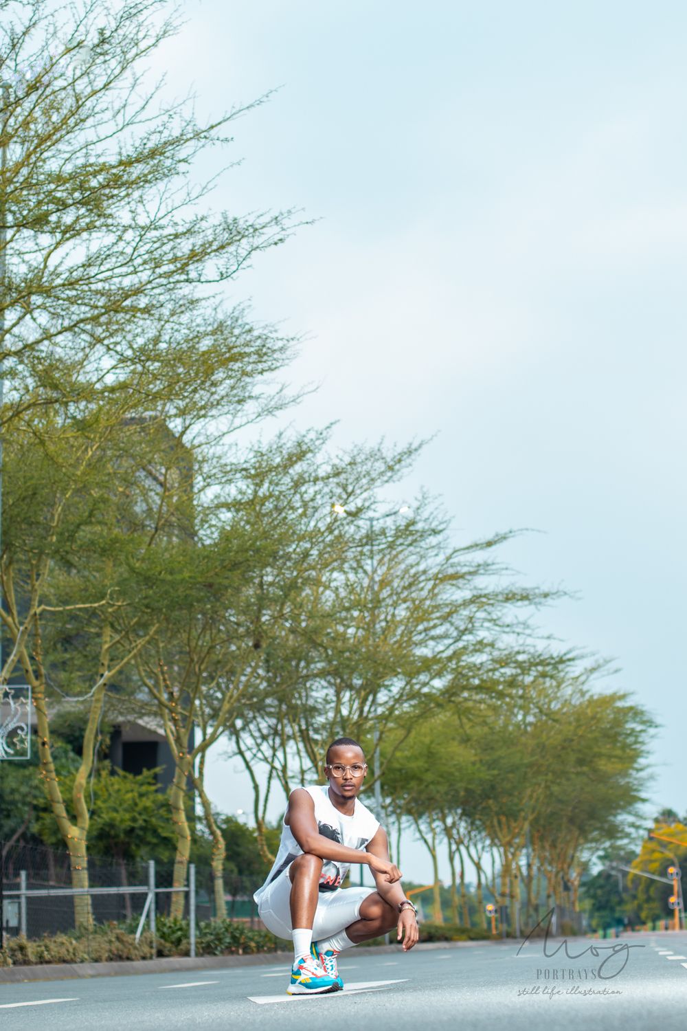 Athletic figure in white crouching on street with trees at sunrise.
