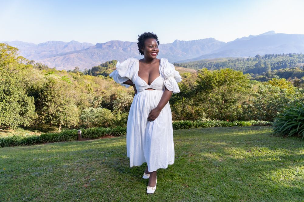 Person in flowing white dress twirls on grassy hilltop with mountains in background.