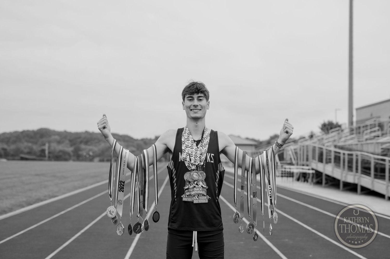 Black and white photo of athlete displaying medals and ribbons on a running track.