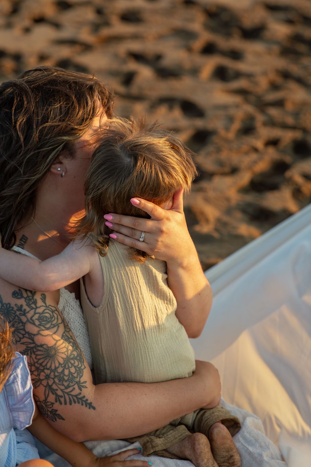 A couple shares an intimate moment on a white blanket at the beach during sunset.