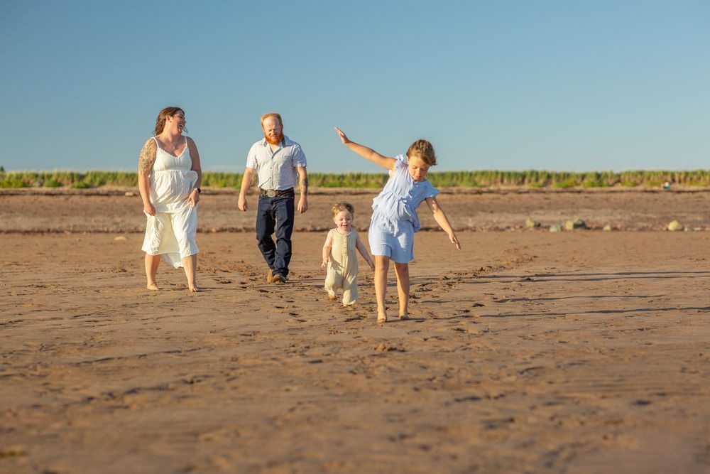 People stroll together on a wide sandy beach with clear blue skies and distant hills in the background.
