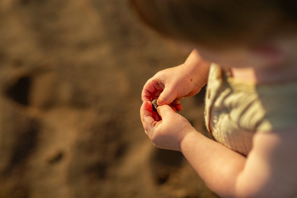 Close-up view of hands holding small red objects against a blurred sandy beach background.