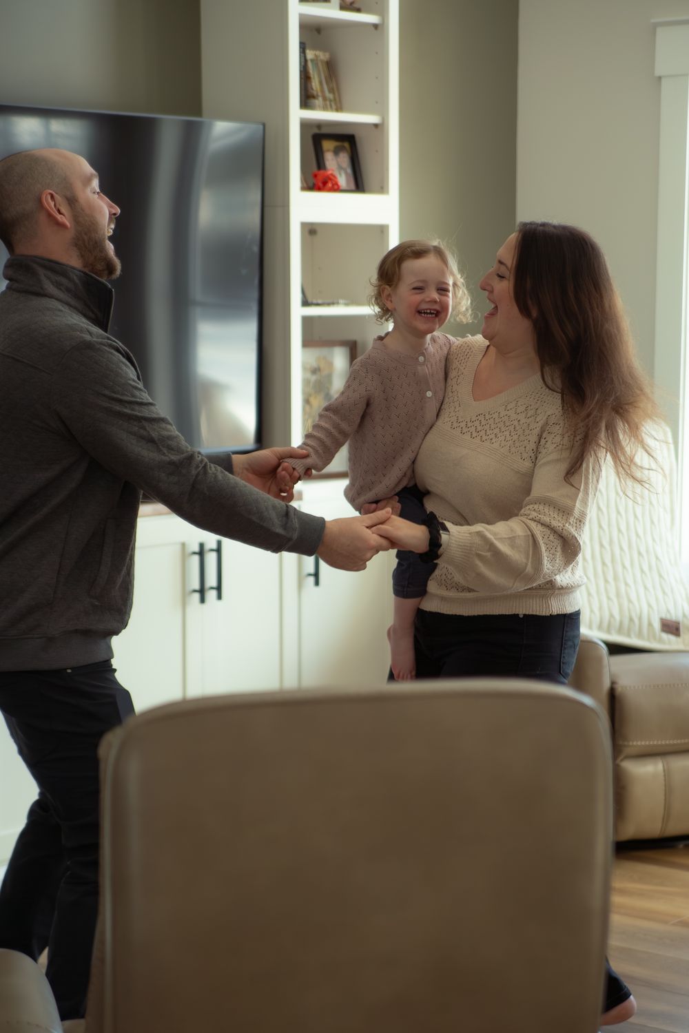 Happy family with young child holding hands and laughing together in a modern living room.