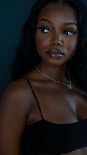 A striking studio portrait of a woman wearing a black top and delicate necklace against a dark background.