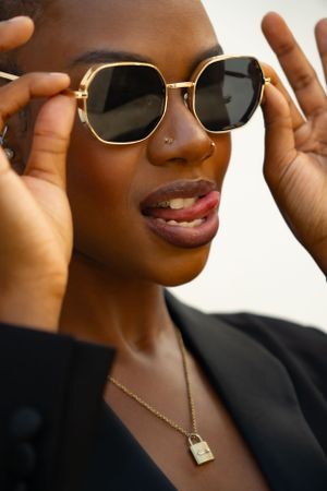 Joyful fashion portrait with gold-framed sunglasses and delicate lock necklace.