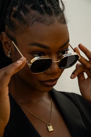 Close-up fashion shot of model adjusting stylish gold sunglasses with lock pendant necklace.