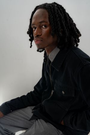 Artistic portrait of person with dreadlocks wearing dark jacket against neutral background.