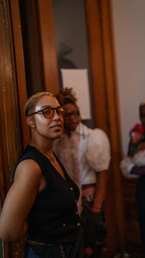 Candid shot of person in black vest and glasses leaning against wooden doorframe.