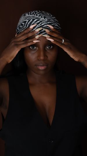 A dramatic portrait of a person wearing a zebra print headwrap and black top with hands framing their face.