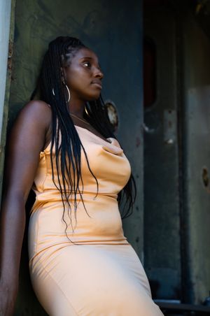 Portrait of someone wearing a peach-colored fitted dress leaning against a wall in soft natural lighting.