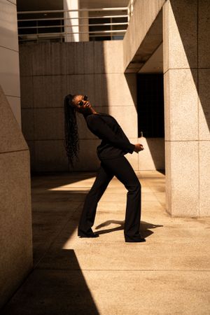 Dancing figure in black attire strikes dramatic pose against concrete architecture with dramatic shadows and lighting.
