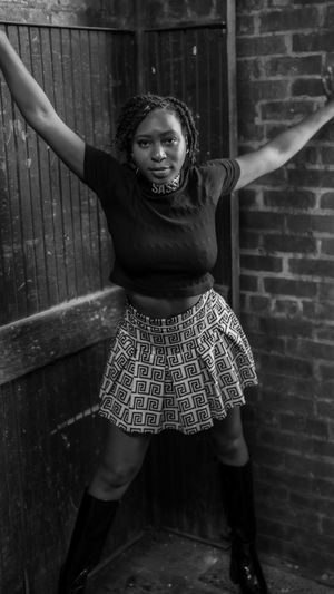 Black and white portrait of a dancer in a patterned skirt striking a dynamic pose against a brick wall.