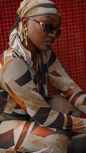 A fashion portrait against red background featuring stylish sunglasses, statement earrings and a patterned outfit.