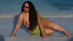 Someone with curly hair in a bikini lounging on a beach with crystal clear blue water on a sunny day.