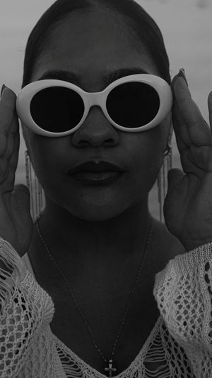 Black and white portrait featuring white sunglasses, lace details, and a delicate cross necklace.
