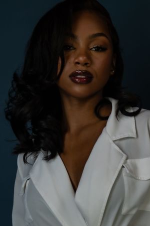 Fashion portrait of woman with dark burgundy lipstick wearing white collar shirt against dark background.