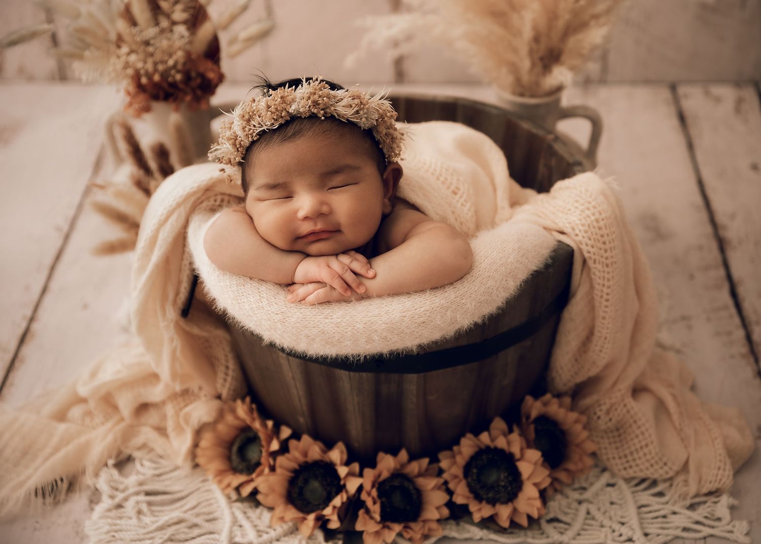 A sleeping baby in a wooden bucket surrounded by sunflowers and soft textures.