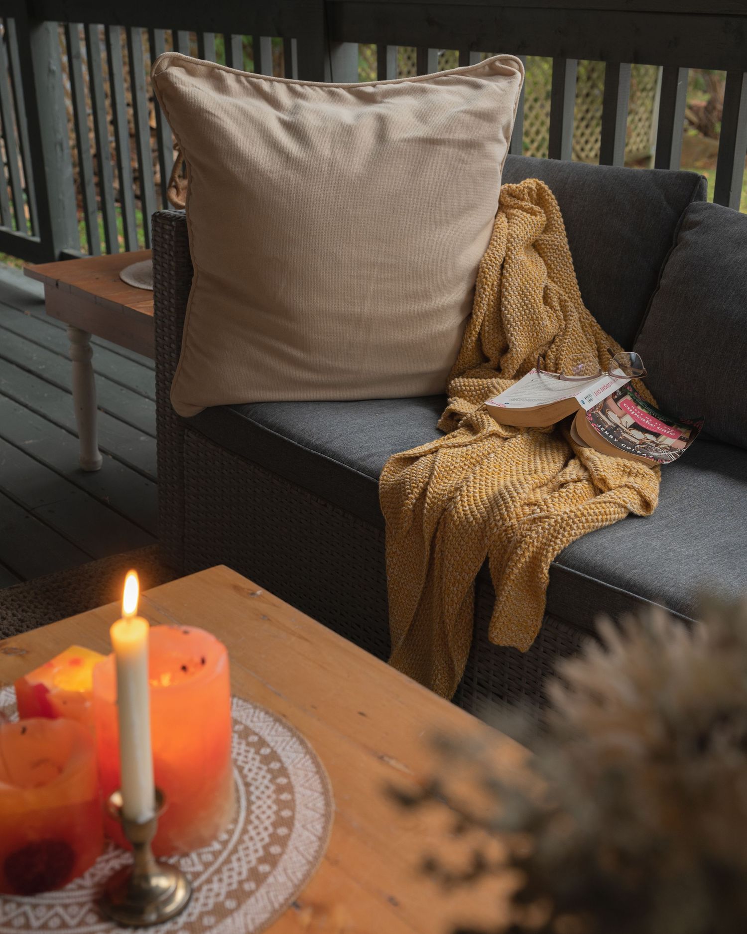 Cozy autumn scene with lit candles, knit throw blanket, and decorative pillow on porch sofa at dusk.