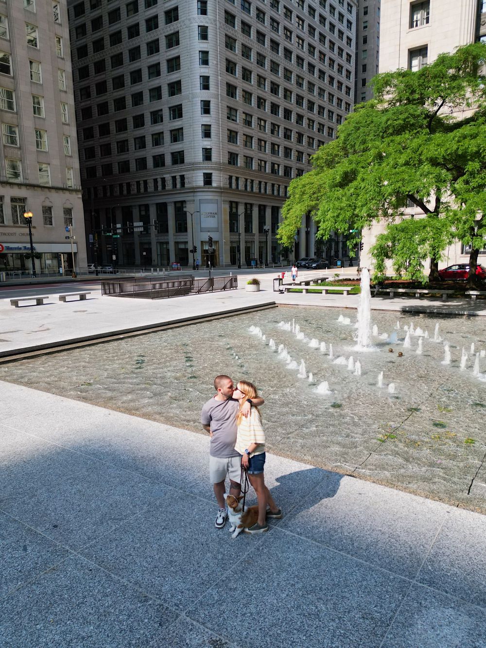 People standing near urban fountain plaza surrounded by modern buildings.