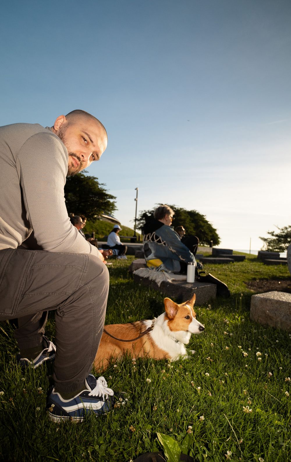 Person sitting outdoors with a Corgi dog on grassy hill during sunset.