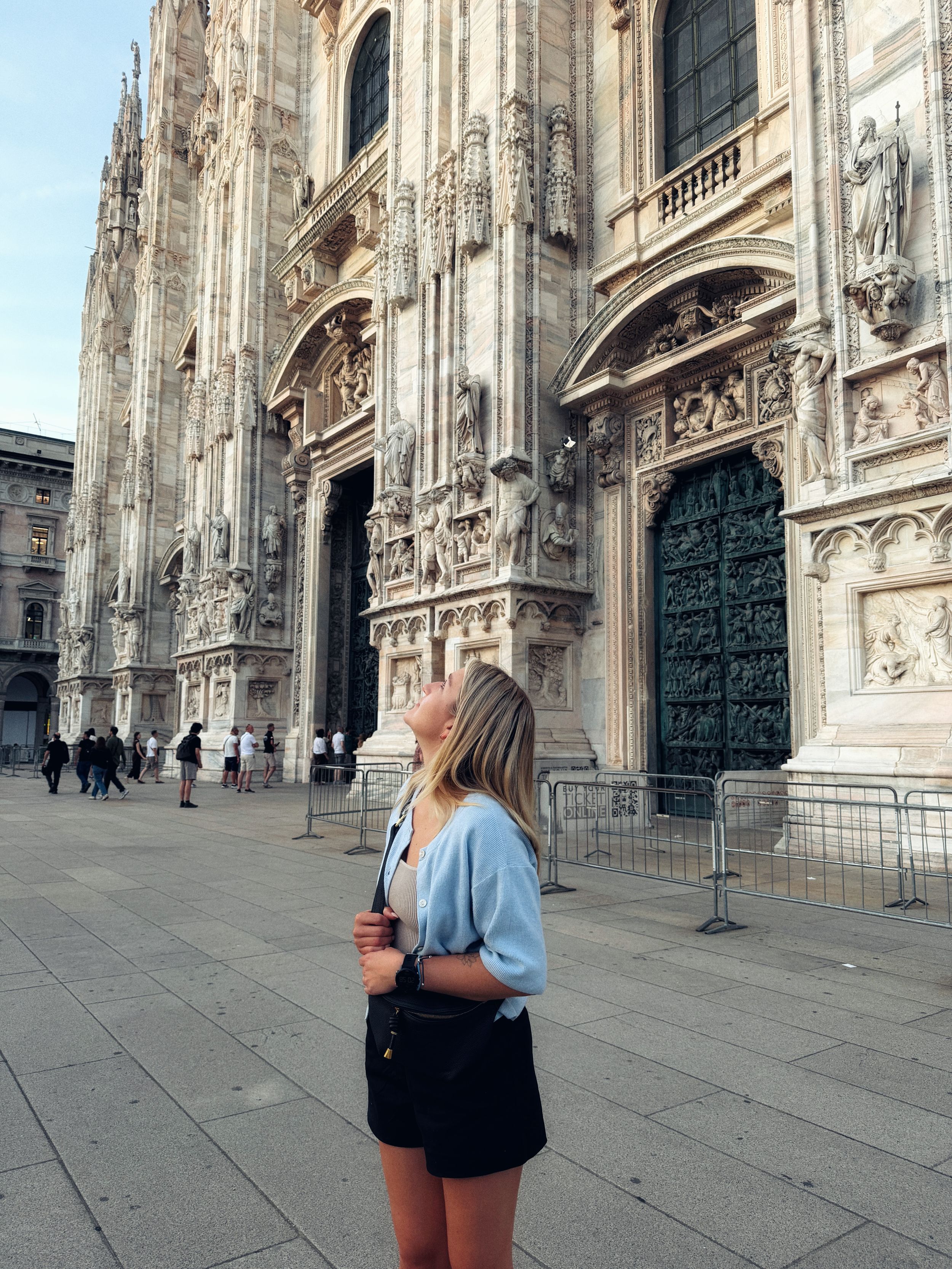 Young woman gazing up at the ornate facade of Milan Cathedral, Duomo di Milano, on a sunny day.