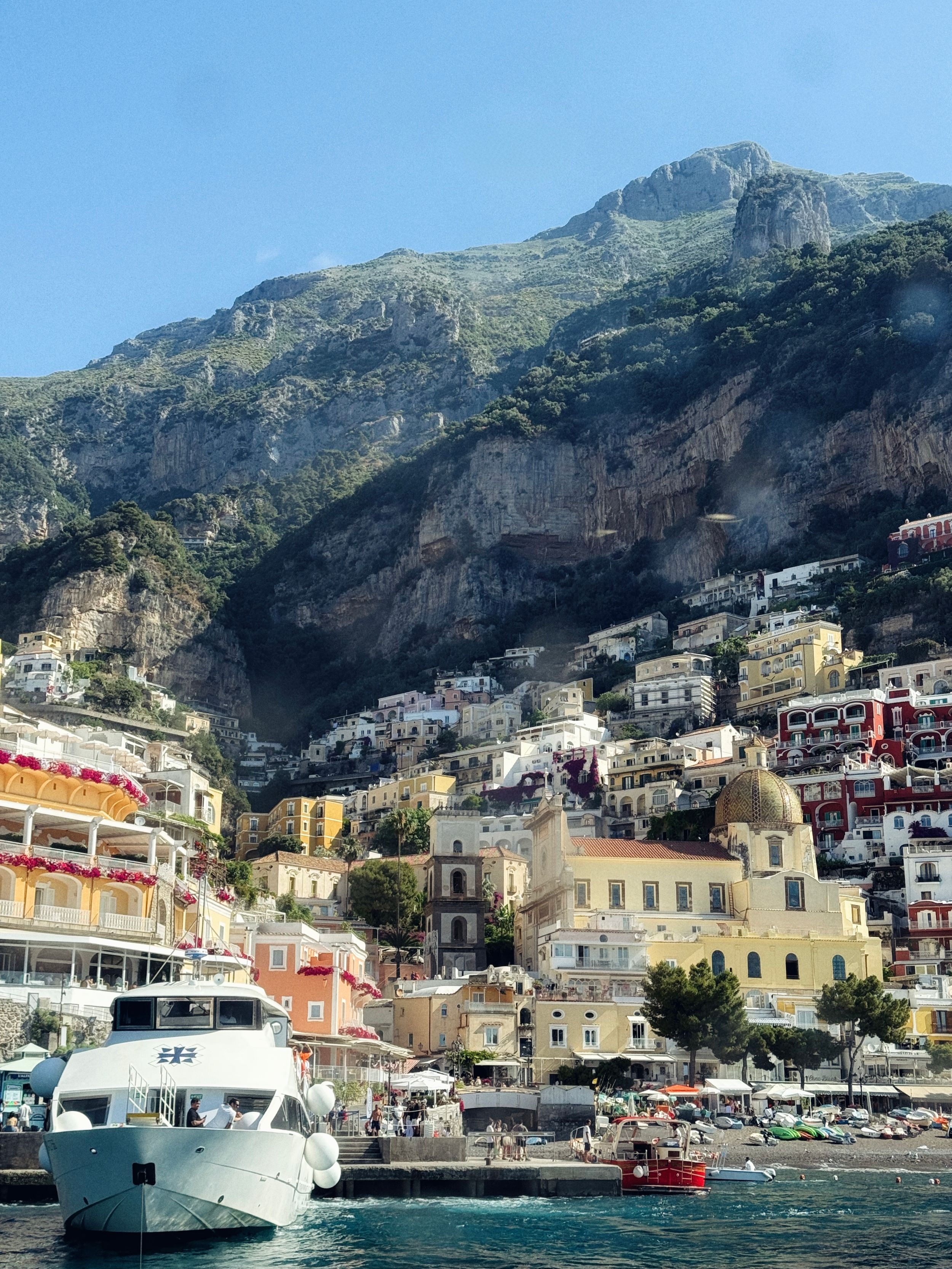 Colorful cliffside buildings of Positano, Amalfi Coast, Italy, with a white yacht docked in the foreground.