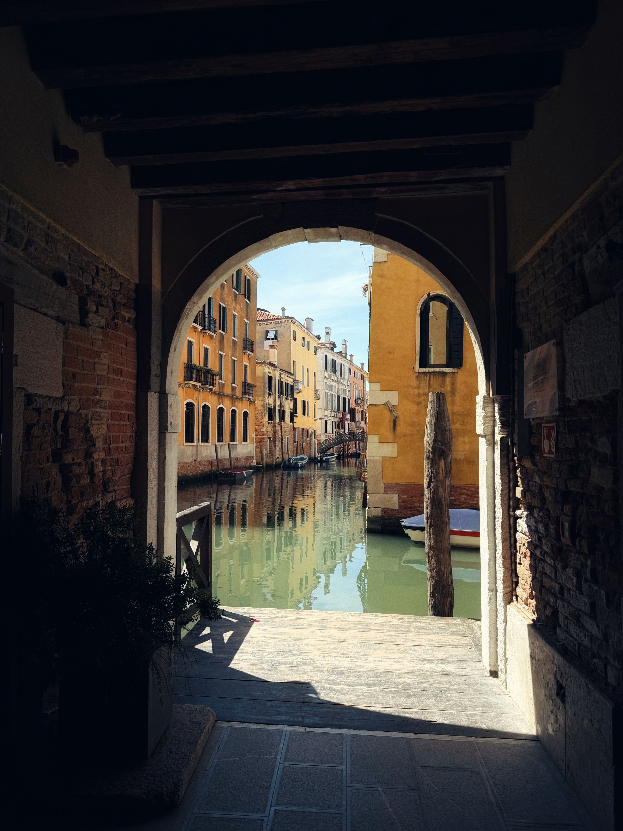 View through a stone archway of a serene Venice canal lined with colorful historic buildings reflecting in calm water.