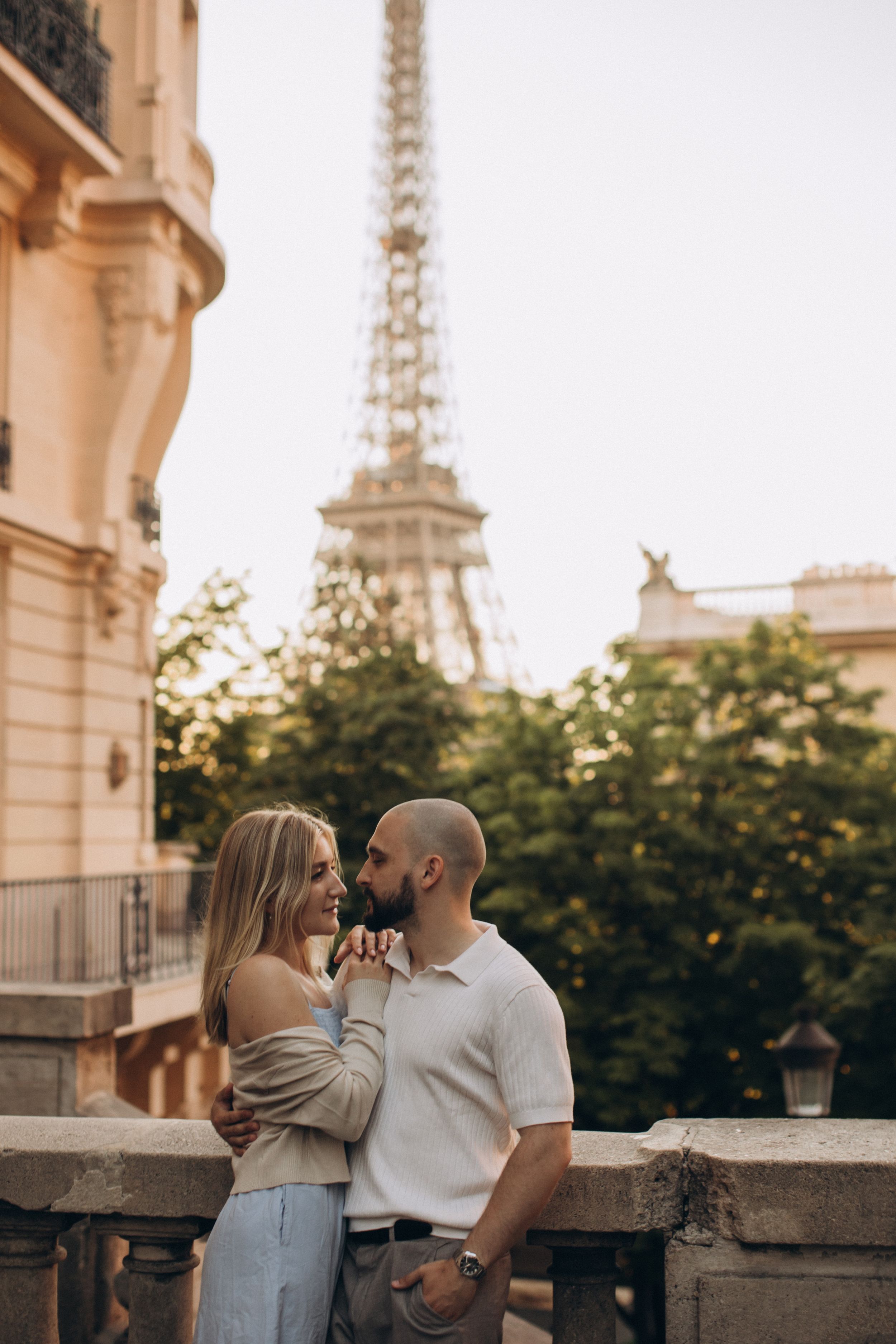 Romantic couple embracing on a Parisian balcony with the Eiffel Tower in the background at golden hour.