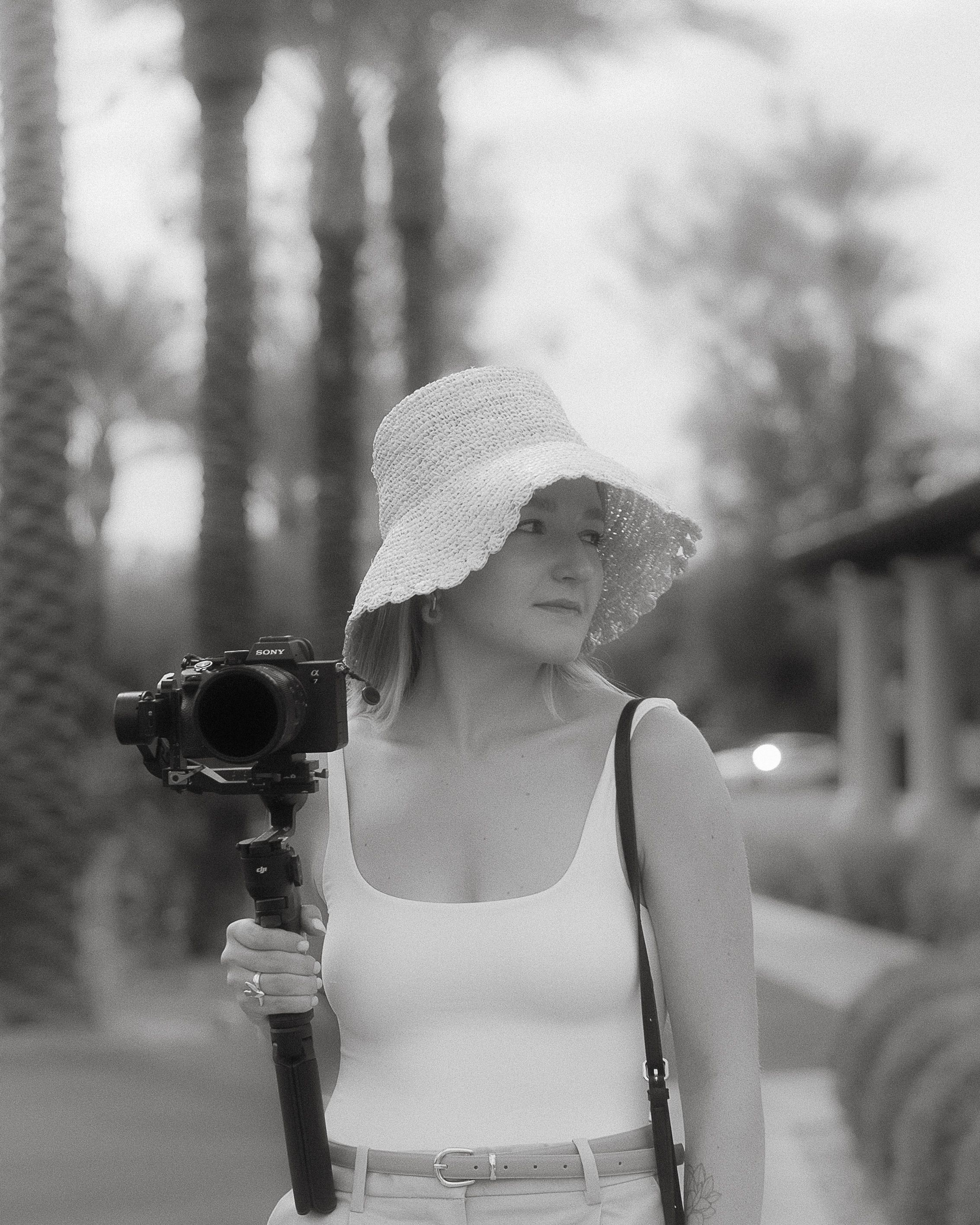 A romantic black and white photo series showing a woman in a white dress and hat walking through a garden setting.
