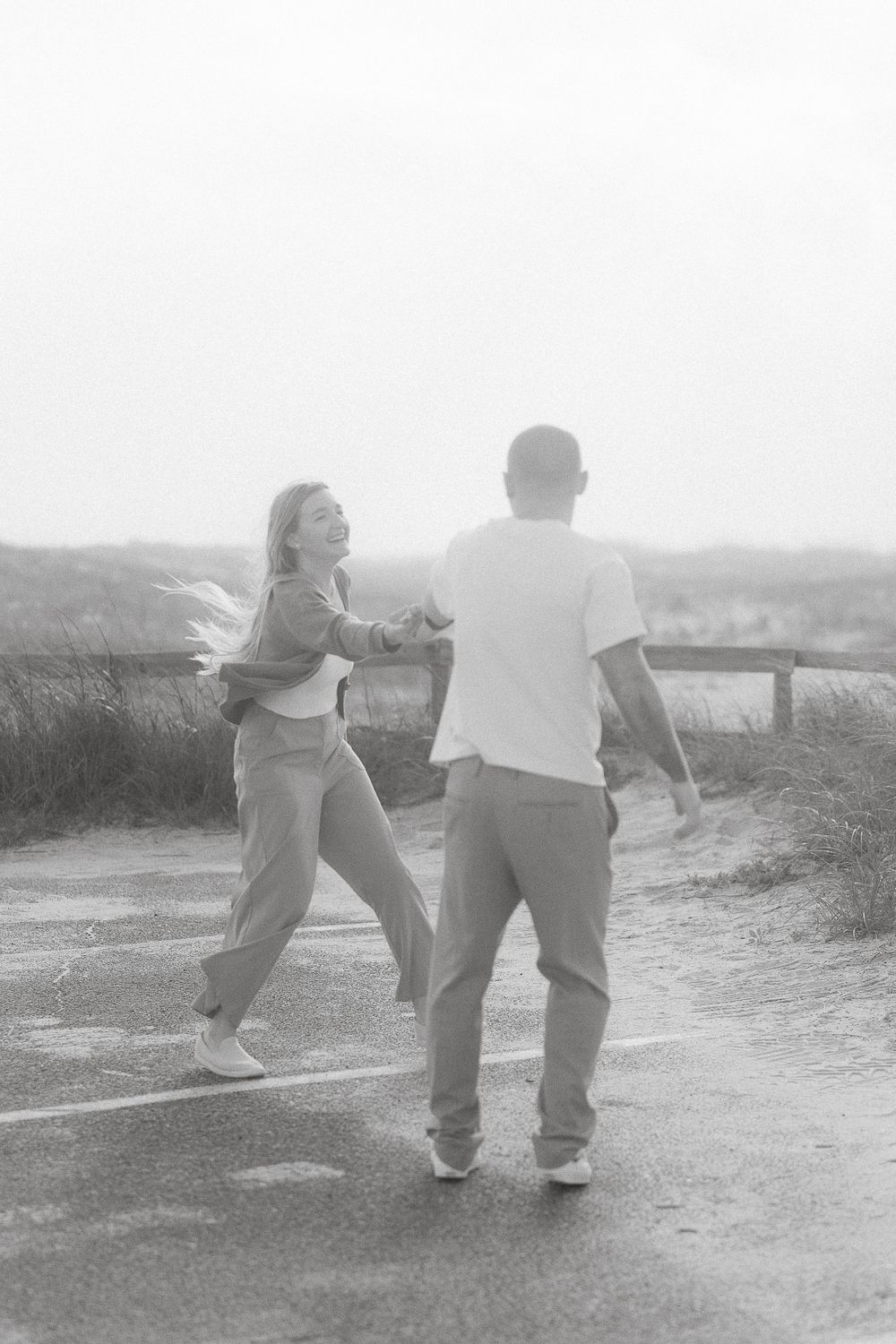 A couple dancing together on a dirt path overlooking a scenic vista in black and white.